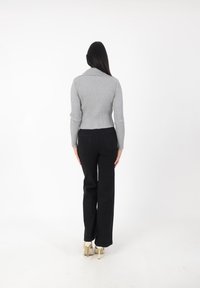 Suéter gris acanalado con cuello doblado, combinado con pantalones negros de cintura alta y tacones blancos. La vista trasera muestra el diseño ajustado y la textura.
