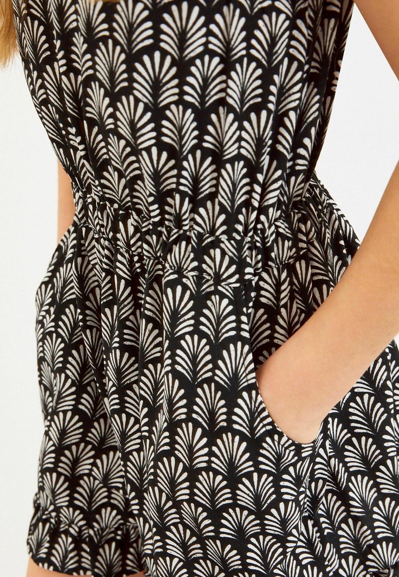 Vêtement en tissu noir avec un motif de fans blancs, doté d'une taille élastique, de poches et de manches froncées. Une vue rapprochée met en évidence les détails.