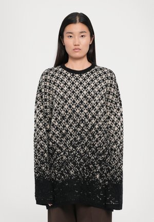 Oversized black and cream sweater with a diamond pattern, featuring a solid black bottom and ribbed neckline. Soft texture with long sleeves.