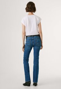 Modr�é džínové kalhoty s přiléhavým střihem, bootcut nohavicemi a dvěma zadními kapsami. V kombinaci s bílou košilí s krátkým rukávem a černými botami na podpatku.