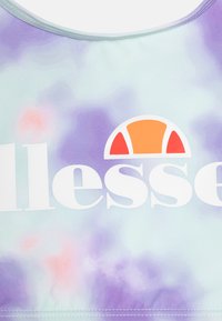 Sportski grudnjak u ljubičastoj i mentol boji s uzorkom tie-dye, s kružnim narančasto-bijelim logom, izrađen od glatkog, rastezljivog materijala s izrezom u obliku polukruga.