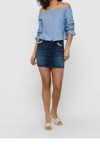 Blusa blu chiaro e bianca a righe con spalline scoperte e bottoni, abbinata a una mini gonna in denim scuro con dettagli decorativi sulle tasche.