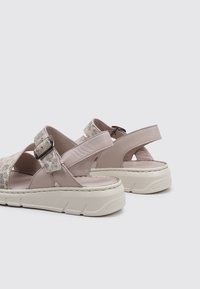 Sandalias rosa claro con correas texturizadas y con patrón, y con hebillas ajustables. Cuentan con una suela blanca gruesa con un ligero relieve para agarre.