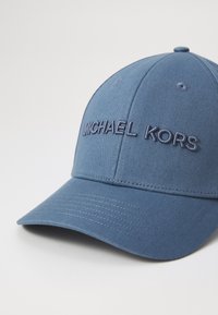Sinine pesapalli müts, mis on valmistatud kangast, esipaneelil tõstetud tikitud "MICHAEL KORS" logoga ja kaardus piiriga.
