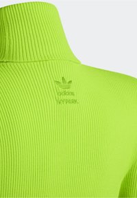 Neongrön ribbad polokrage med en upphöjd logotyp med texten "Adidas IVY PARK" på ryggen. Slät textur med en figurnära design.