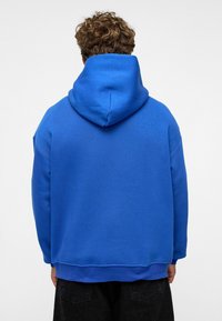 Blauwe katoen hoodie met een grote, verstelbare capuchon, geribbelde mouwen en een relaxte pasvorm; zachte textuur en minimale ontwerpdetailleringen.