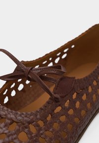Chaussure plate en cuir tressé marron avec un nœud noué sur le dessus et un motif découpé sur les côtés.