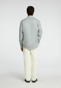 Camicia azzurro chiaro a maniche lunghe con una vestibilità comoda, polsini con bottoni e colletto, abbinata a pantaloni bianchi a gamba larga e scarpe nere.