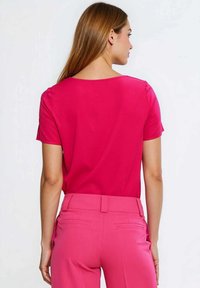 Krótki rękaw, top z okrągłym dekoltem w jasnoróżowym kolorze, wykonany z gładkiej tkaniny, zestawiony z dopasowanymi różowymi spodniami z tylnymi kieszeniami.