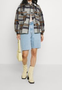 Geruite wollen jas in grijs, paars en oranje, met twee borstzakken. Gecombineerd met lichtblauwe spijkershort en beige laarzen met vierkante neus.