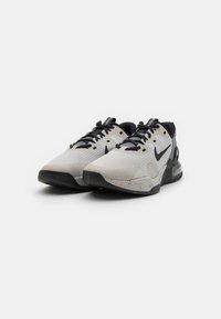 Nike Sportschuhe aus hellgrauem Mesh mit schwarzen Akzenten. Verfügt über eine strukturierte Laufsohle, prominente Air-Dämpfung und ein Schnürdesign.