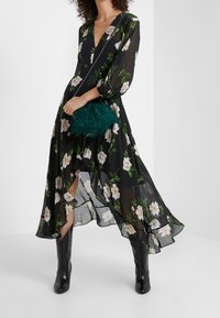 Zwarte bloemen maxi-jurk van doorschijnende stof, met witte bloemen en groene bladeren. Vergezeld van een donzige teal handtas en zwarte enkellaarsjes.