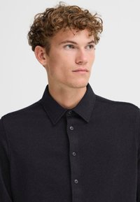 Camicia da uomo grigio scuro con colletto, abbottonatura e tessuto texturizzato. Presenta una vestibilità comoda e dettagli di cucitura sottili.