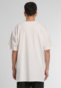 Short-sleeve, oversized t-shirt in cream cotton. Features a crew neck and relaxed fit, with visible stitching along the collar and hem.