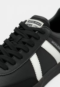 Black sneaker with white side stripes, black laces, and "JACK & JONES" branding on tongue and side panel.