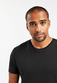 Tricou negru cu guler rotund, fabricat dintr-un material de bumbac neted, având mâneci scurte și un design ajustat, fără modele sau grafica vizibile.