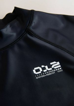 Melna auduma izstrādājums ar augstu apkakli, pie šuves atrodas balts uzdrukāts teksts "012 SYSTEM REBOOT 1000".