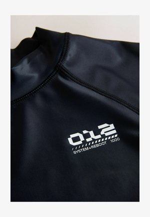 Črna tkanina z visokim ovratnikom, na šivu je bel natisnjen napis "012 SYSTEM REBOOT 1000".