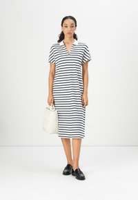 Stripet kjole med V-hals, korte ermer, til kneet, i hvit og marineblå. Kombinert med en kremfarget vevd håndveske og svarte loafers.