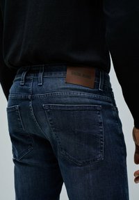 Granatowe dżinsy o teksturowanym wykończeniu. Charakteryzują się brązową skórzaną naszywką z napisem "SALSA JEANS" oraz klasycznymi tylnymi kieszeniami.
