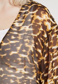 Lichtgewicht, doorschijnende kimono in een bruine en gouden dierenprint. Voorzien van een diepe halslijn en vloeiende mouwen met fijne stikdetails.