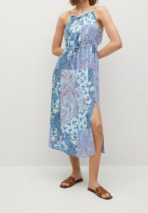Maxikleid mit blau-rosa Muster, Rüschenausschnitt, verstellbaren Trägern und einem seitlichen Schlitz. Getragen mit braunen flachen Sandalen.