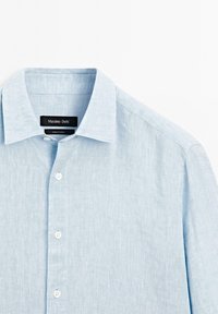Chemise en lin bleu clair avec une texture douce, col pointu et six boutons blancs le long du devant. L'étiquette indique "Massimo Dutti."