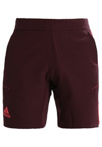 Mörk vinröda Adidas sportshorts med subtil prickig mönster, elastiskt midjeband och röd Adidas-logotyp på vänster ben.