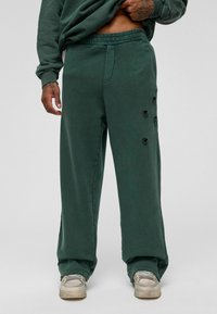 Groene broek met wijde pijpen van textuur katoen, met versleten accenten aan één kant en een elastische tailleband voor comfort.