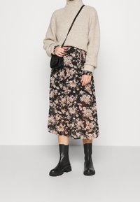 Beżowy sweter dzianinowy, spódnica midi w czarnym kolorze z różowym kwiatowym wzorem, czarne skórzane botki za kostkę oraz mała czarna torebka na ramię.