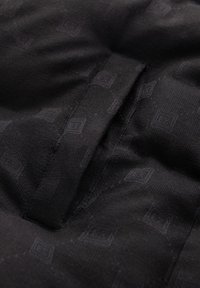 Svart tyg med ett subtilt mönster av små geometriska former. Texturen verkar slät med svaga sömnadsdetaljer längs sömmarna.