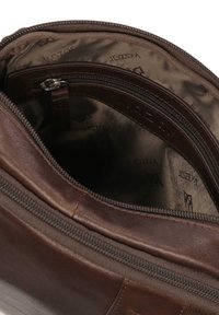 Interior de bolso de cuero marrón con un bolsillo con cremallera y forro de tela suave con un patrón de logo repetido. Costuras visibles y detalle en la cremallera.