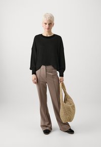 Pulover negru cu nervuri, pantaloni largi bej cu pliuri în față, asortați cu o geantă bej matlasată și pantofi cu talpă înaltă negri.