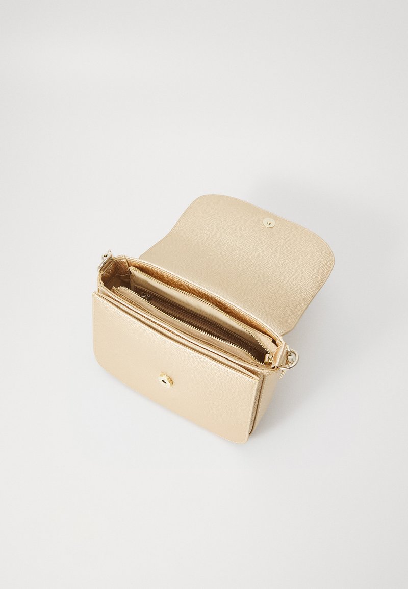 Sac à main en cuir beige avec un rabat, doté d'un fermoir à pression doré et de deux compartiments intérieurs avec des détails zippés. Fini texturé.