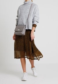 Jasnoszary, dziergany sweter z kołnierzem typu turtleneck, brązowa midi sukienka w kwiaty, białe sneakersy oraz szara torebka na ramię z srebrnym zapięciem.