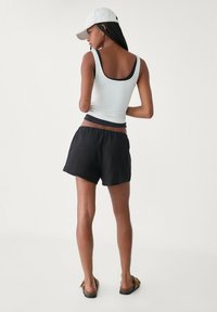 Lichtblauw, aansluitend tanktop met een zwarte afwerking, gecombineerd met losse zwarte shorts en sandalen. De persoon staat met een witte pet en gevlochten haar.