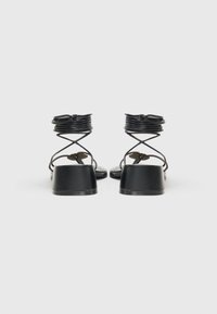 Sandalias de tacón negro con diseño de punta cuadrada, correas texturizadas que se envuelven alrededor del tobillo y un resistente tacón cuadrado.