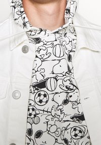 Felpa con cappuccio bianca con disegni a linee nere di personaggi dei cartoni animati e articoli sportivi, dotata di chiusura con coulisse e tessuto testurizzato.