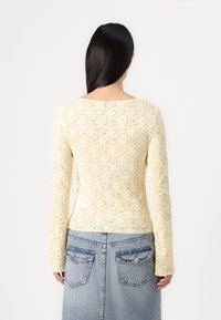 Spets långärmad topp i ljusgul, med ett blommönster och rundad halsringning, i kombination med en denimkjol med fickor.