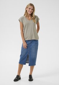 Haut vert olive à manches courtes et décolleté en V associé à une jupe en denim longueur genoux avec une fente à l'avant, portée avec des mocassins noirs.
