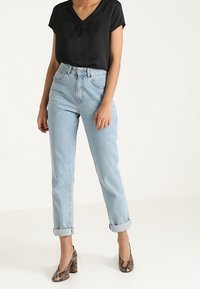 Top nero a maniche corte con pizzo, jeans a vita alta blu chiaro e scarpe con tacco a fantasia. Bordo risvoltato sui jeans.