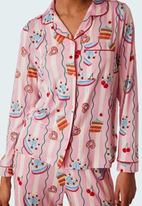 Rosa pyjamaset med mönster av tårtor och körsbär, med en knäppt skjorta med lång ärm och matchande randiga byxor. Mjuk tygtextur.