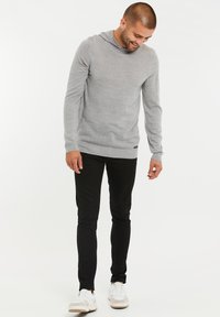 Grijze hoodie met lange mouwen en een geribbelde onderkant, gedragen met zwarte slim-fit broek en witte sneakers. Schoon, minimalistisch ontwerp.