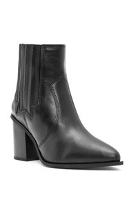Bota de tobillo de cuero negro con punta afilada, tacón apilado y paneles elásticos verticales. Textura suave con costuras y acentos mínimos.