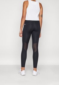 Mustat urheilulegginsit, joissa on verkkomaisemaisia paneeleita pohkeissa, joustava vyötärö ja pieni Nike-logo takana. Kevyt kangas.