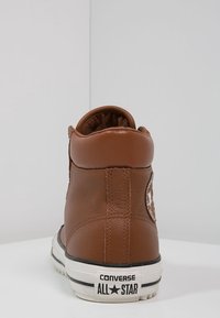 Brown leather high-top sneaker featuring white rubber sole and logo patch, with stitched detailing and padded ankle support.