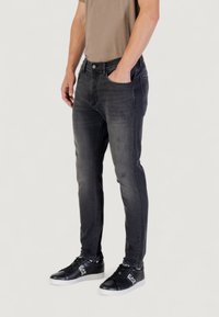 Jeans en denim noir avec une coupe slim, un léger délavage et une légère détérioration, associés à des baskets noires montantes. Design texturé et décontracté.