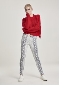 Pull en tricot rouge, coupe cropped ; jean slim blanc avec motif serpent bleu ; accompagné de baskets blanches.