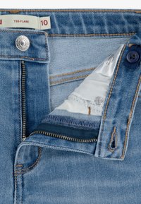 Hellblaue Denim-Jeans mit einem Schlagdesign, Reißverschluss und kontrastierenden Nähten. Das Etikett zeigt Größe 10 und Modellnummer 726 an.
