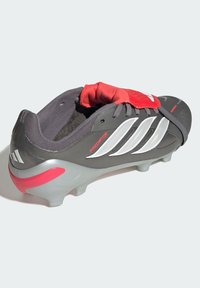 Bota de fútbol gris con rayas blancas y detalles rojos, con una parte superior texturizada, cuello acolchado y diseño de suela flexible.